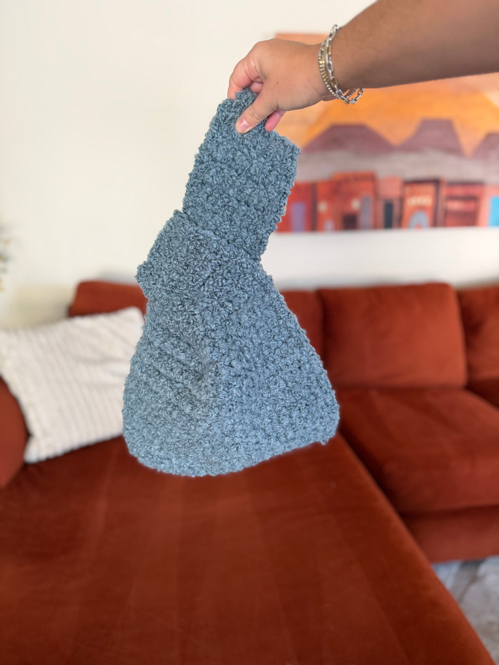 Crocheted blue Japanese knot bag in front of blurred orange couch