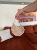 A hand holding a mini shell crochet bag with a gold chain in front of a blurred orange couch