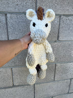 white and grey crochet unicorn in front of brick wall