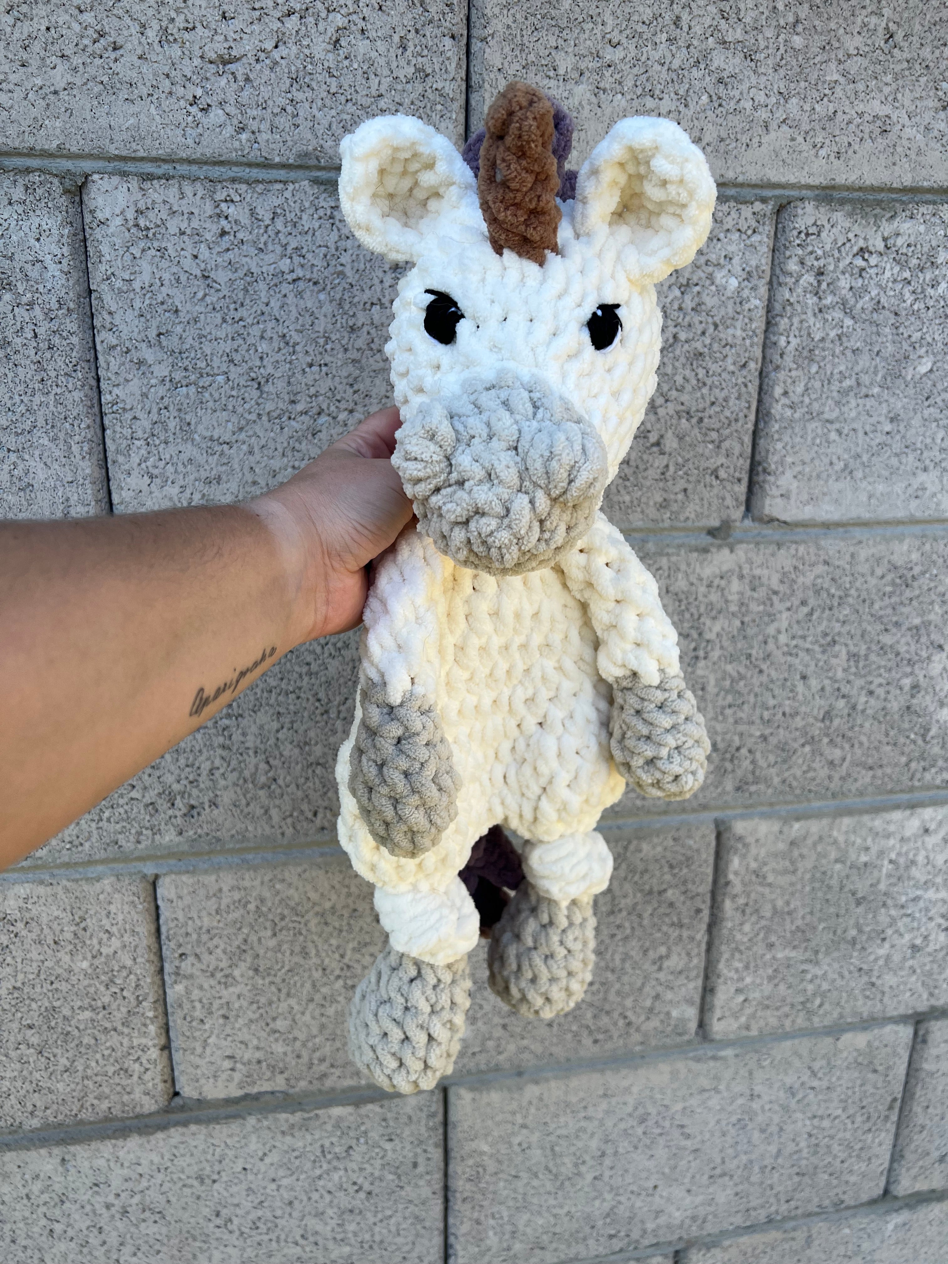 white and grey crochet unicorn in front of brick wall