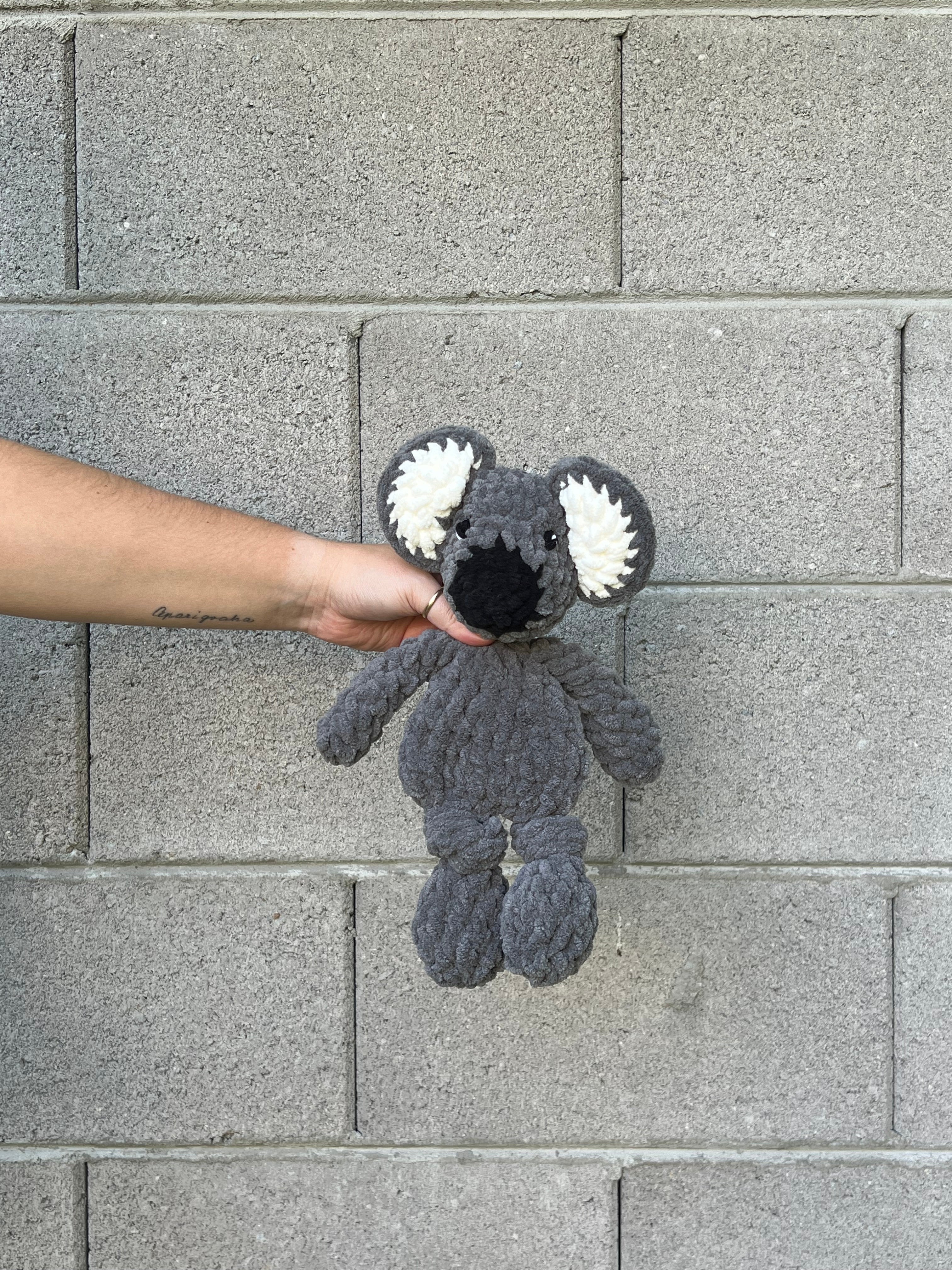 grey crochet koala in front grey brick wall
