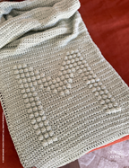 Green M bobble crochet blanket on orange background