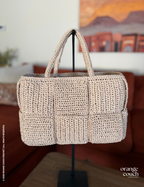 Beige crochet woven handbag on stand in front of blurred orange couch