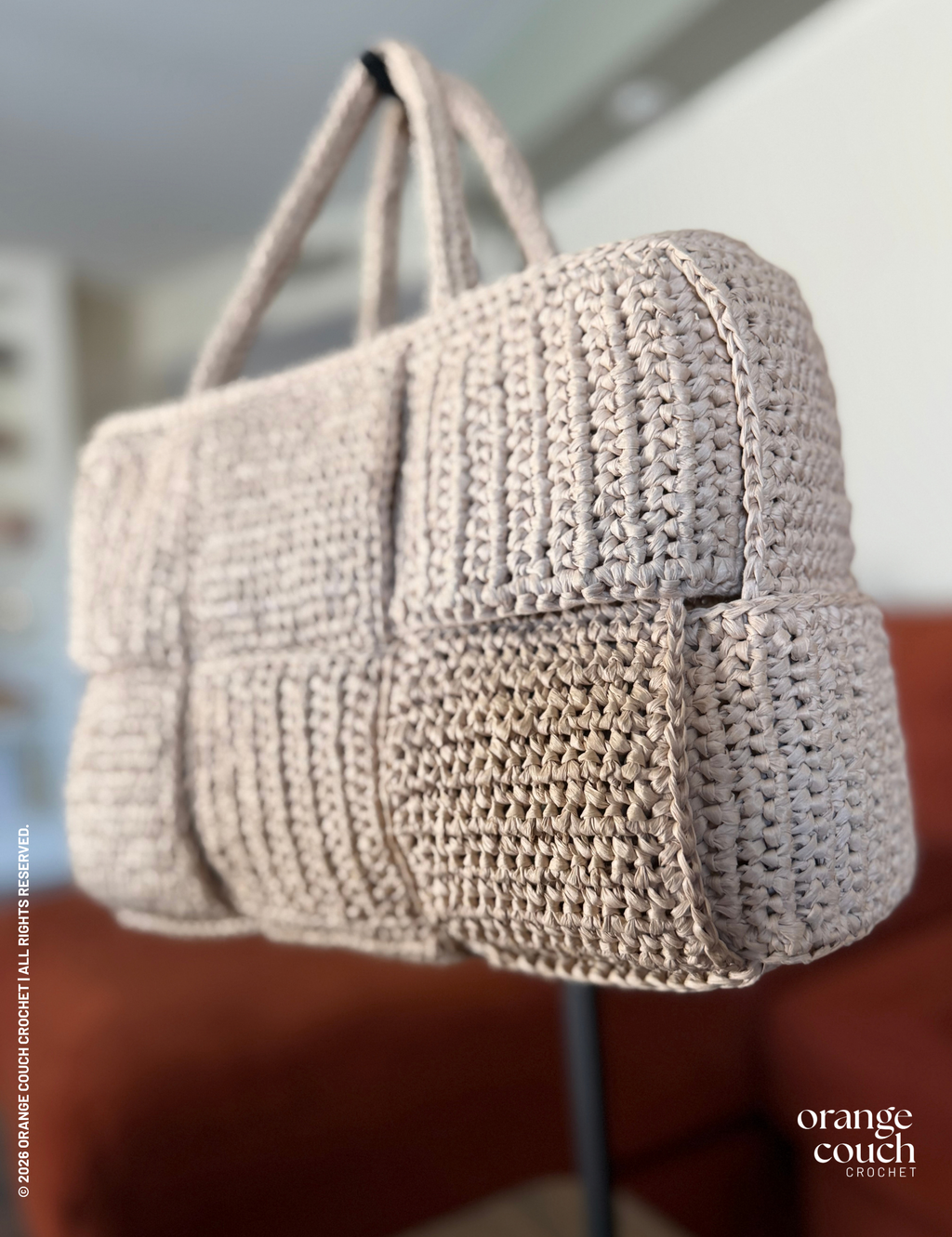 Beige crochet woven handbag on stand in front of blurred orange couch